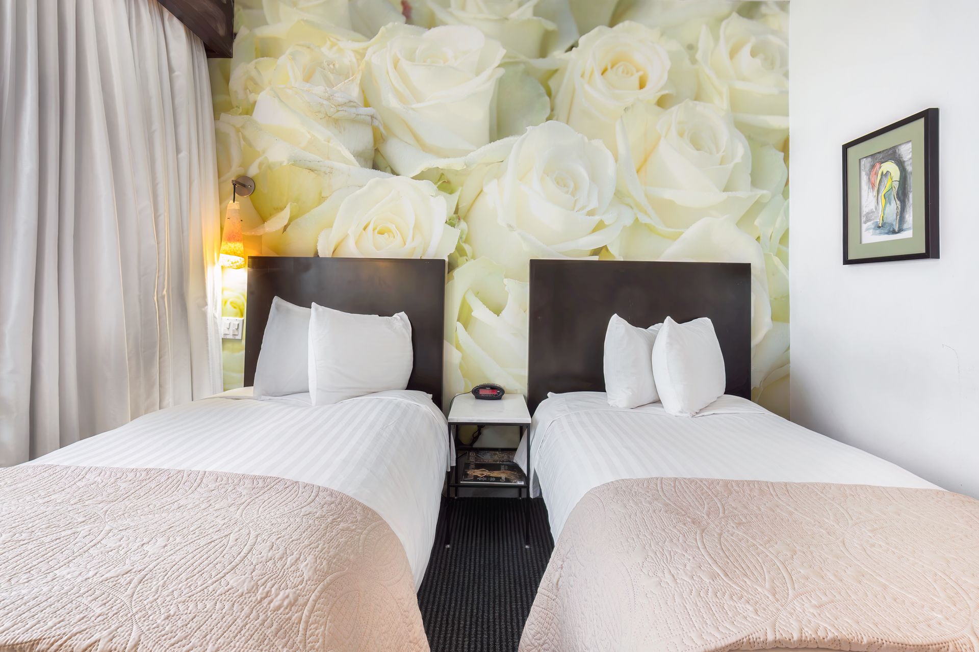 A hotel room with two beds and a mural of white roses on the wall.