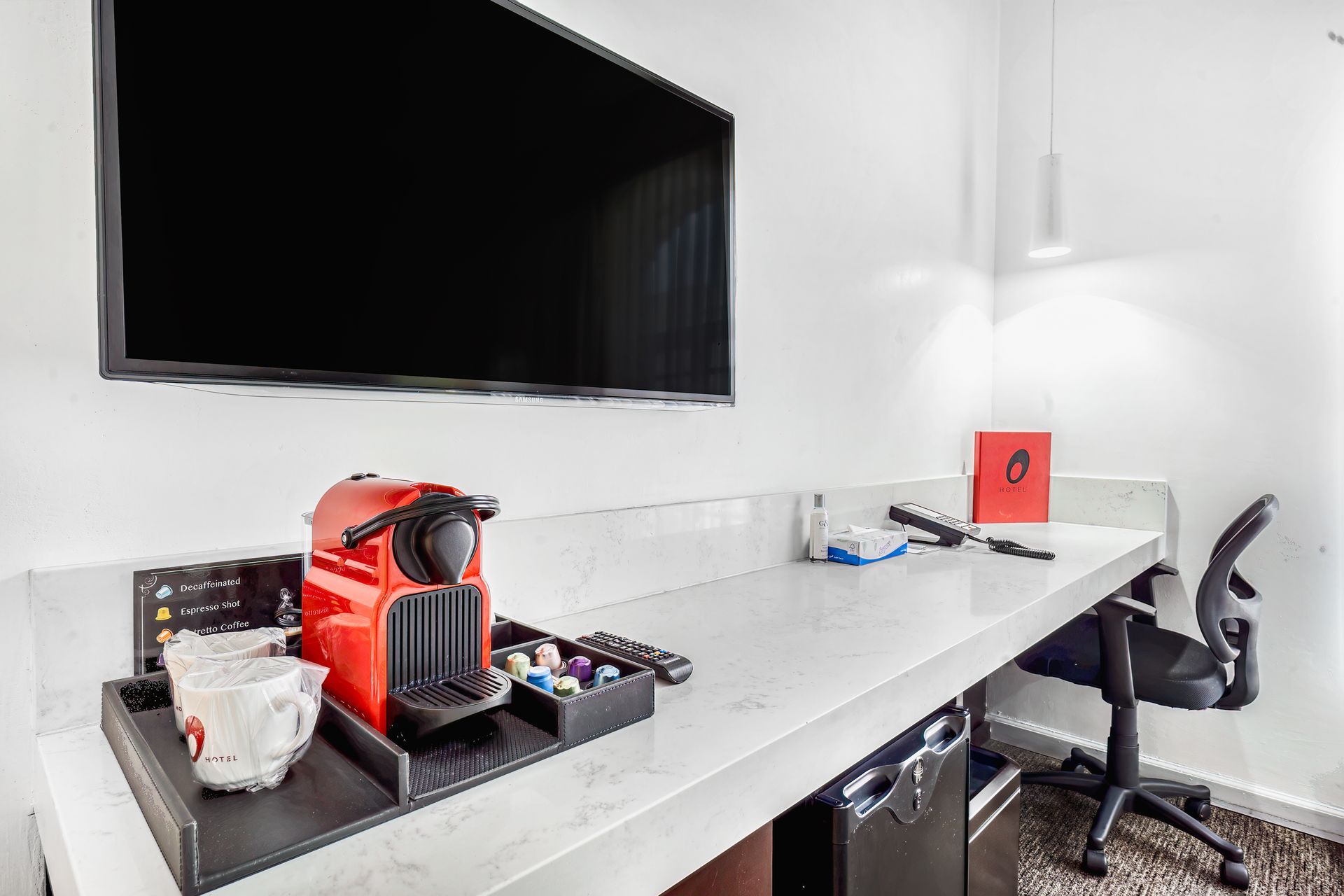 A hotel room with a desk , chair , coffee maker and television.