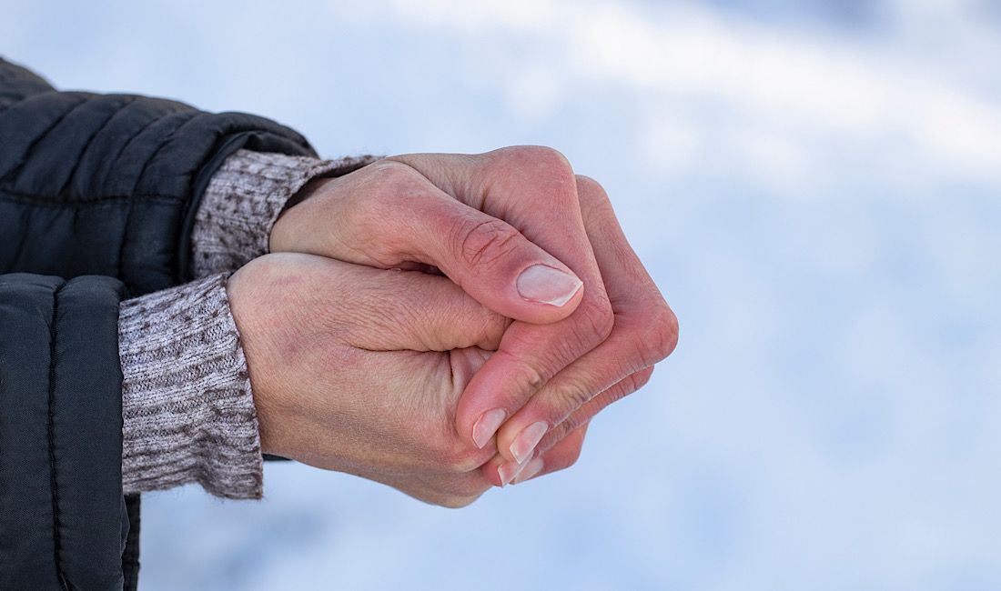 Female holding hands together to keep warm, experiencing hypothermia in the cold winter
