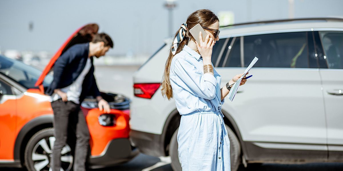 Auto accident, man and woman. Woman filing a car accident claim with insurance. Man perplexed and examining damaged car.