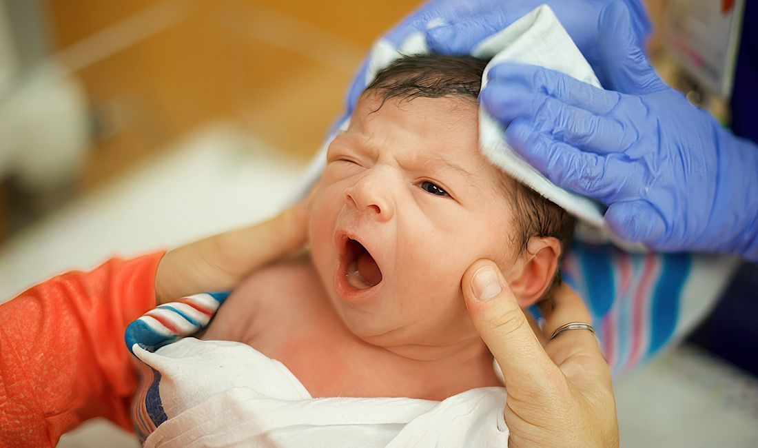Newborn baby getting cleaned up with gauze while mother and nurse are holding him.