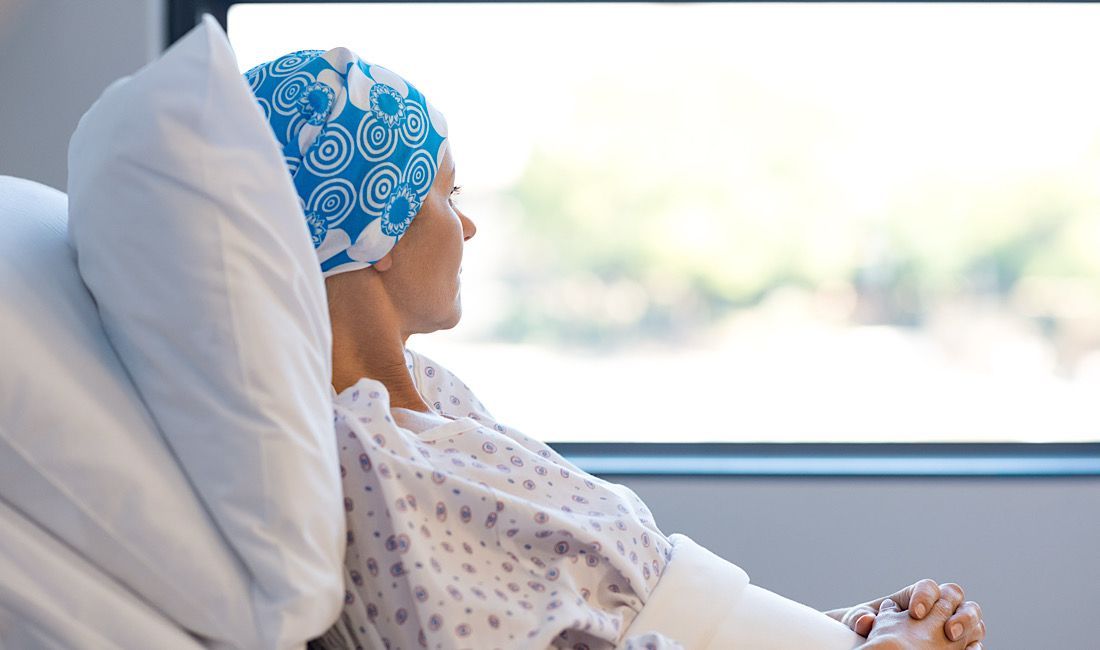 Cancer patient staring at the window with hair cap on.