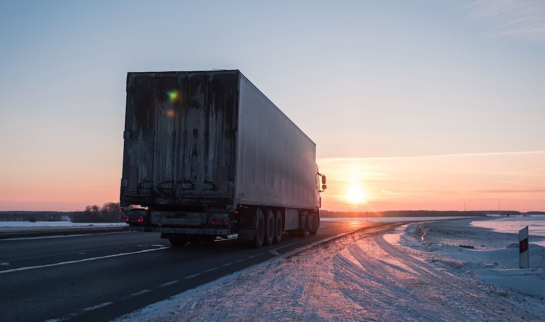 Commercial truck driving on the Pennsylvania interstate during the winter. Surrounded by snow, ice, and the sunset.