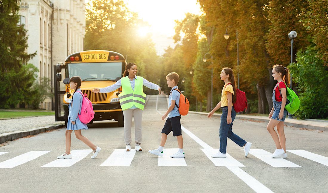 Students walking on crosswalk to school with bus behind them and crossing guard getting them to safe