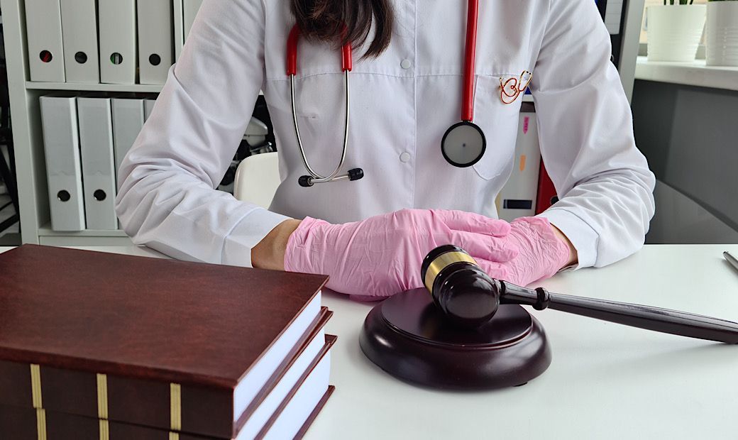 female doctor sitting at table with surgical gloves on next to a law book and a gavel