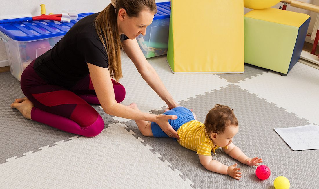 Infant suffering from birth injury now has to partake in rehab treatment. Female physical therapist helping baby with birth trauma recovery,