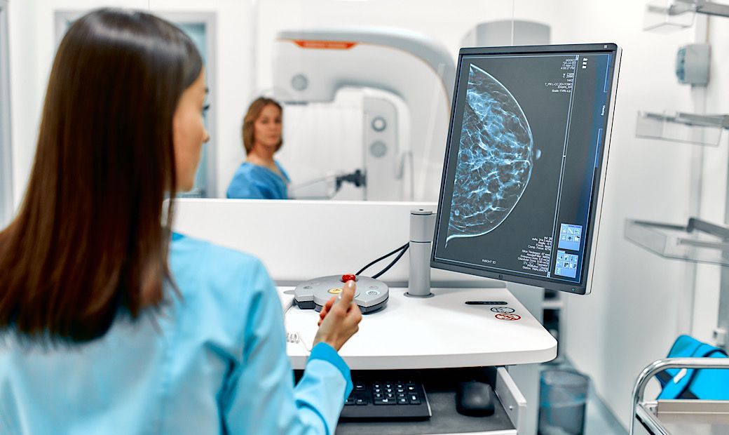 radiology technician performing mammogram on middle-aged female