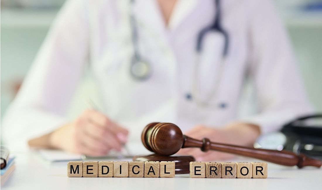 Doctor sitting at a desk writing patient notes behind a gavel and words stating the medical error in Pittsburgh, PA.