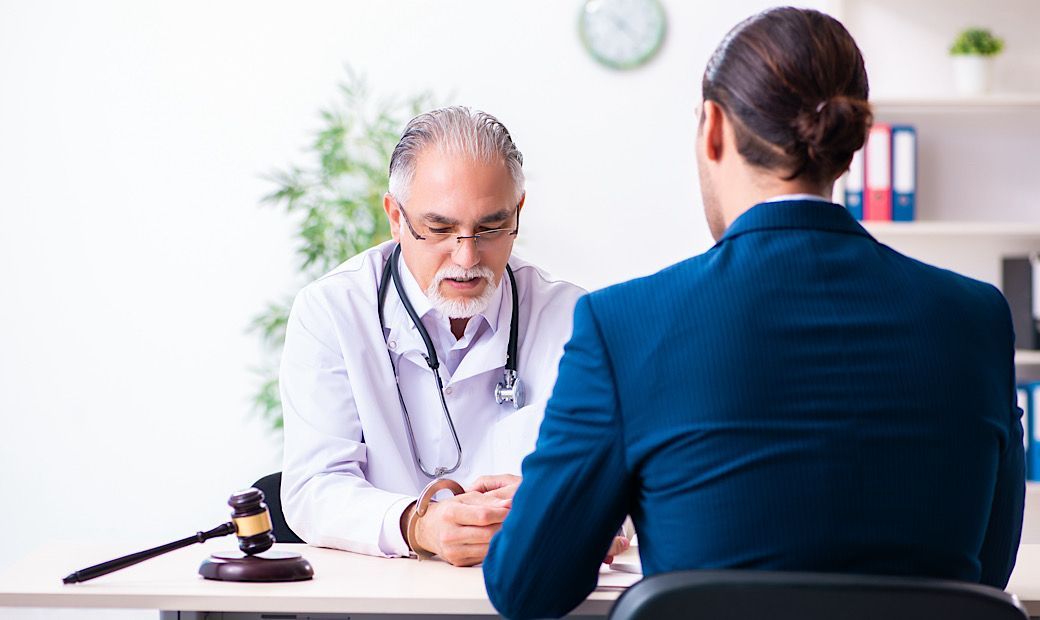 doctor in hand cuffs sitting at a table with a medical malpractice lawyer