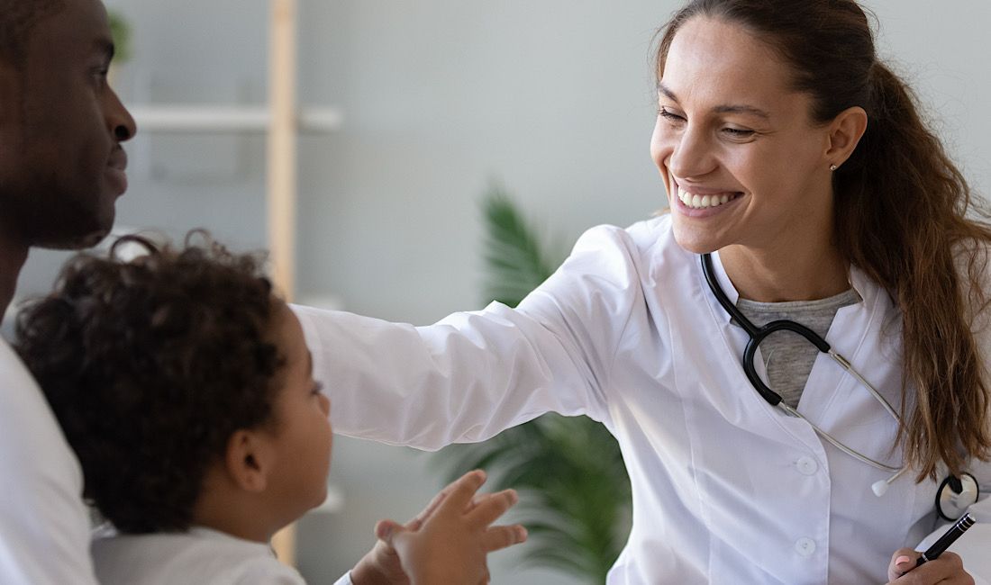Nurse practioner smiling at pediatric patient who is sitting next to their dad.