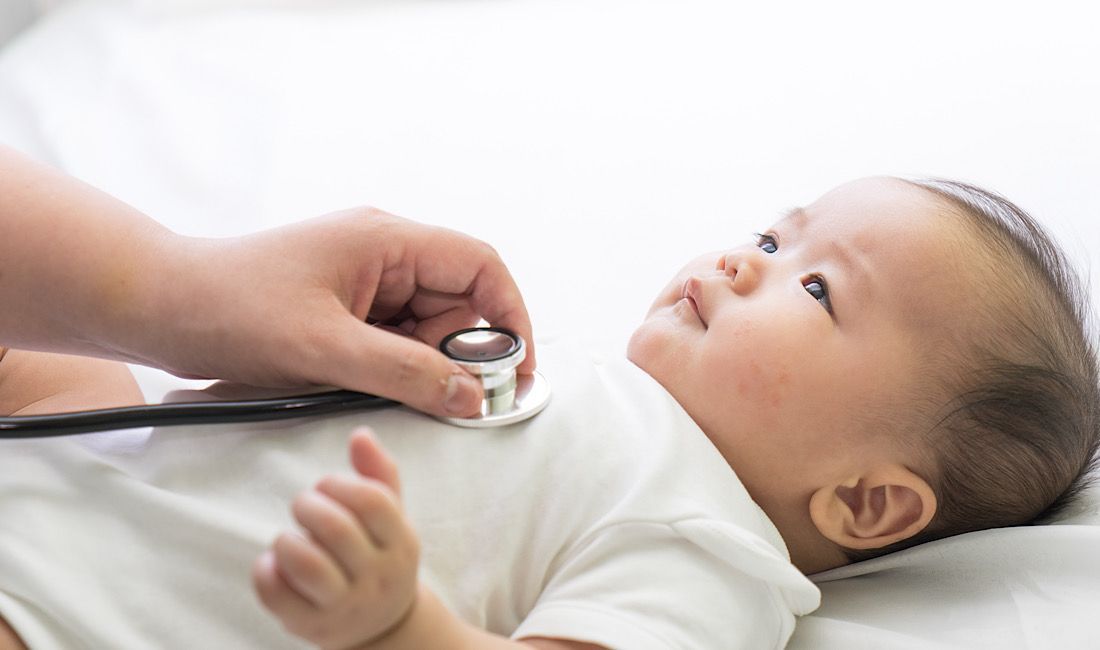 Sweet newborn getting his heart checked out. Infant at the doctors office, stethoscope on chest.