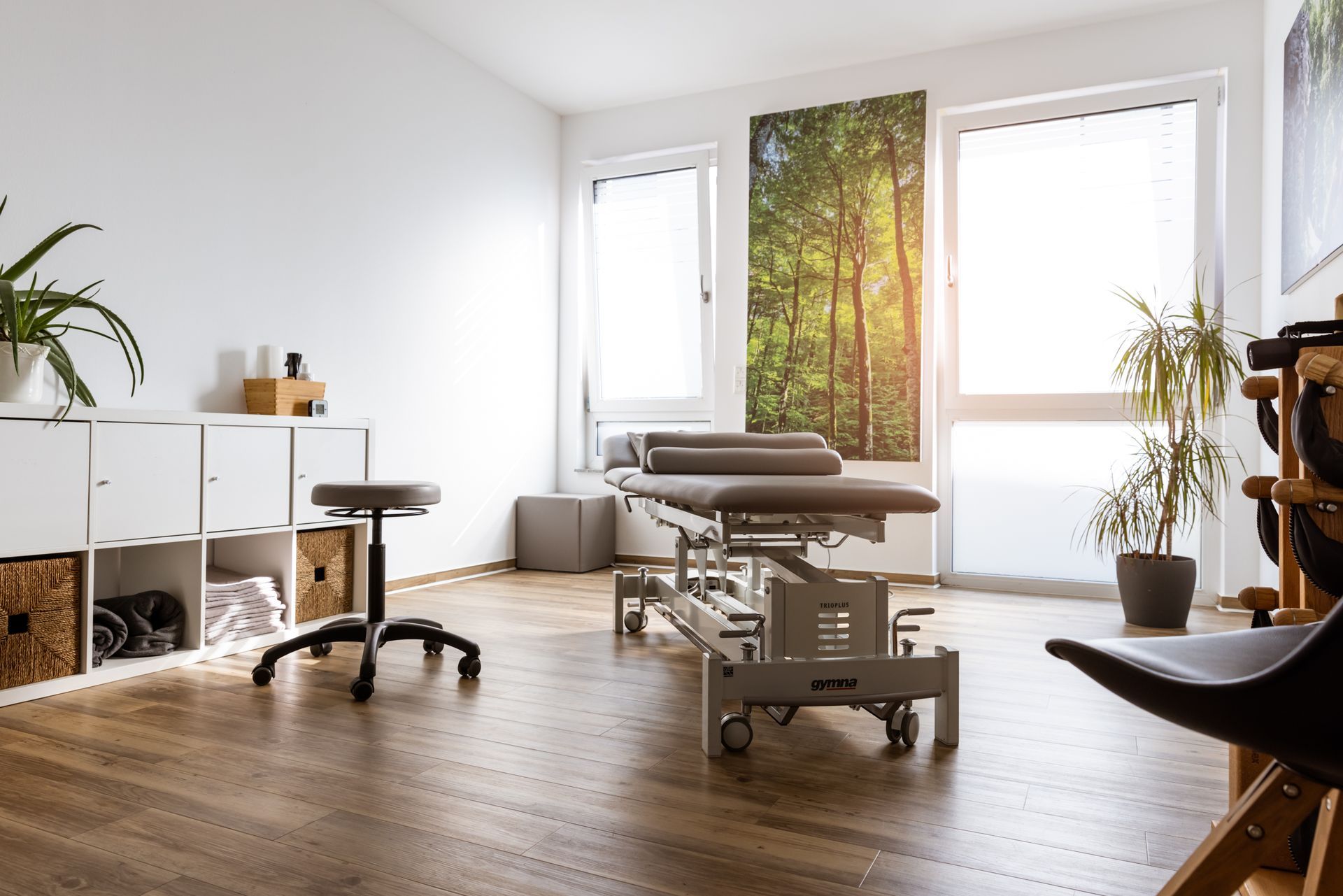 Ein heller Behandlungsraum mit großen Fenstern und Holzparkett