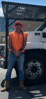A man in an orange vest and hat is standing next to a truck.