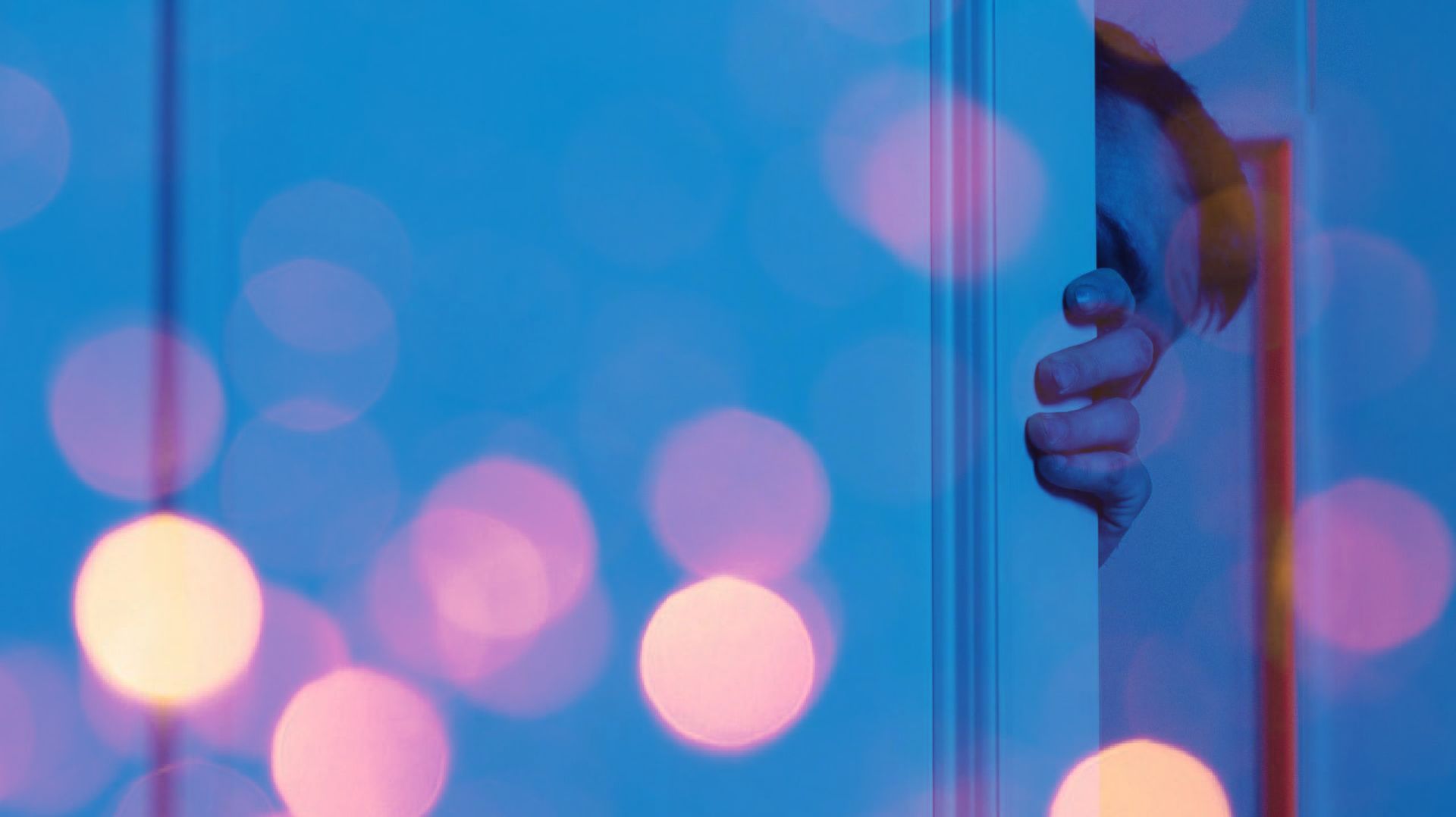 A person is peeking out from behind a glass door.