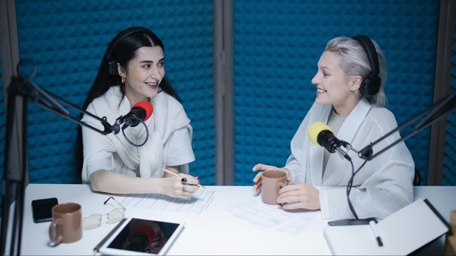 Two women are sitting at a table talking into microphones.