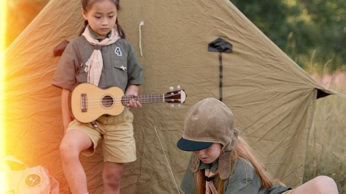 two young girls are playing ukuleles in front of a tent .