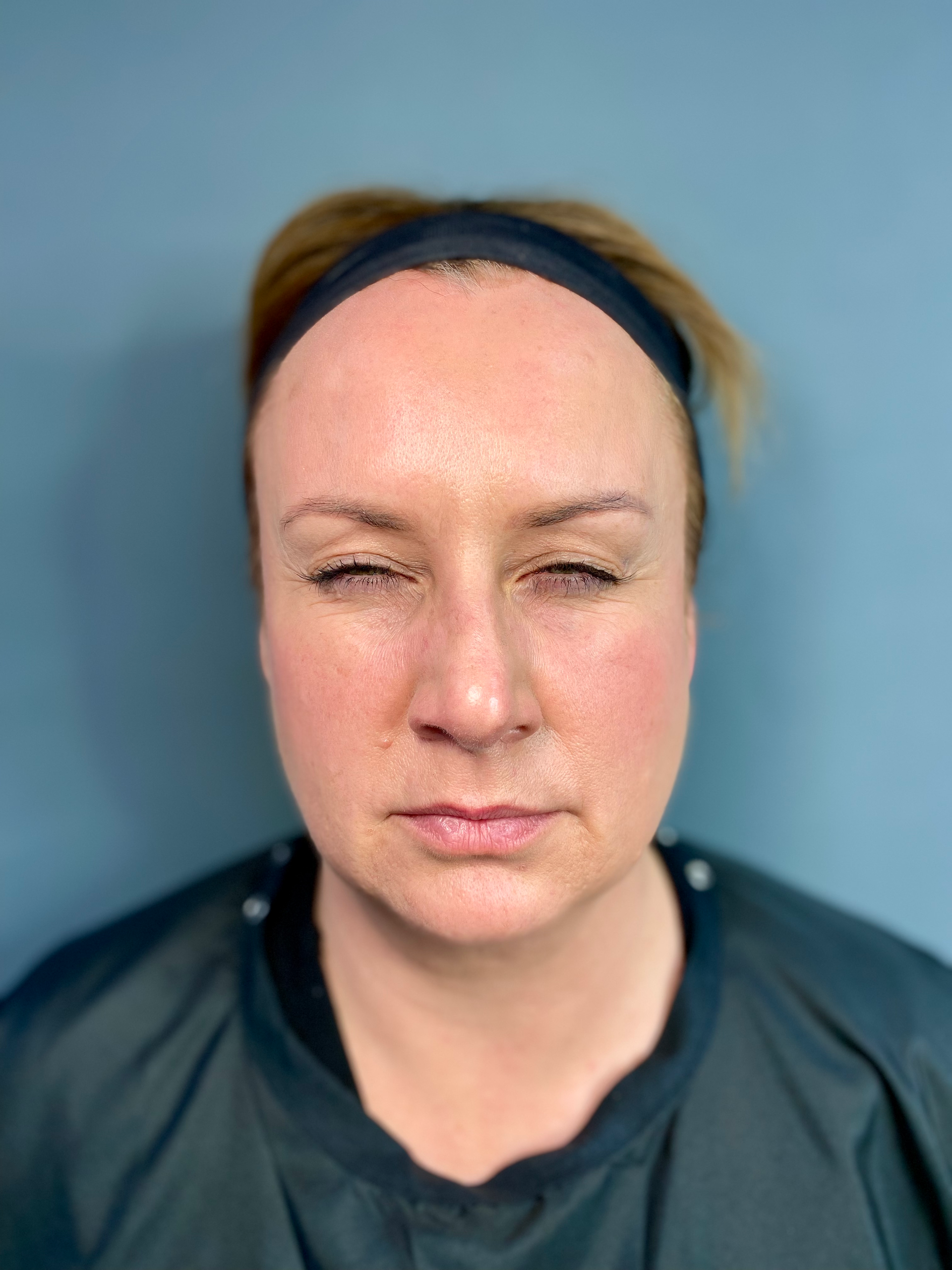 A woman with a headband on her head is looking at the camera with her eyes closed.