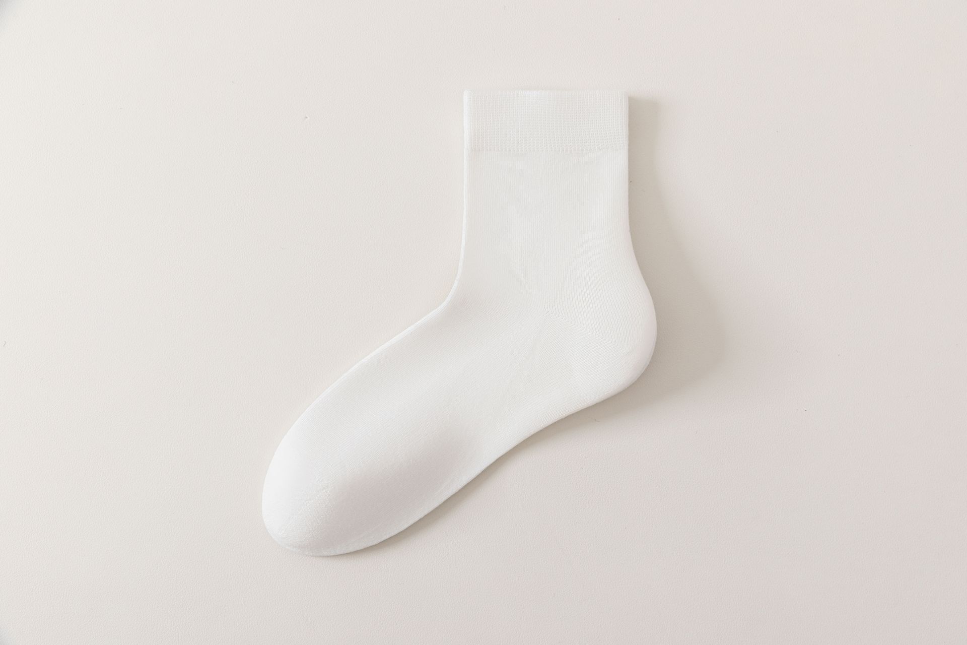 Person relaxing, holding glass of water, wearing white socks, in modern white space.