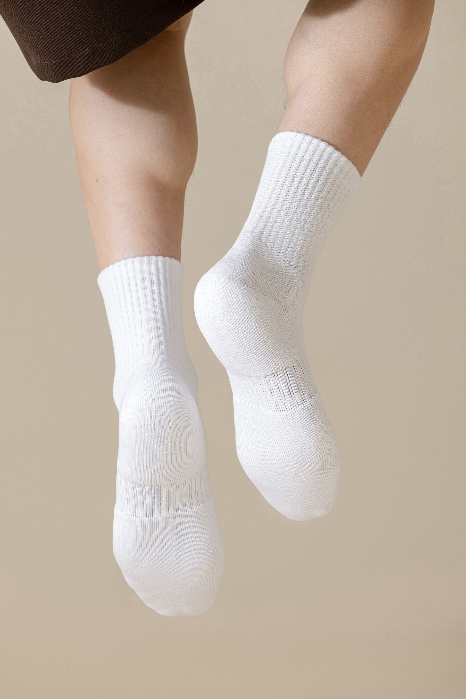 Pair of white socks on legs, against a tan background.