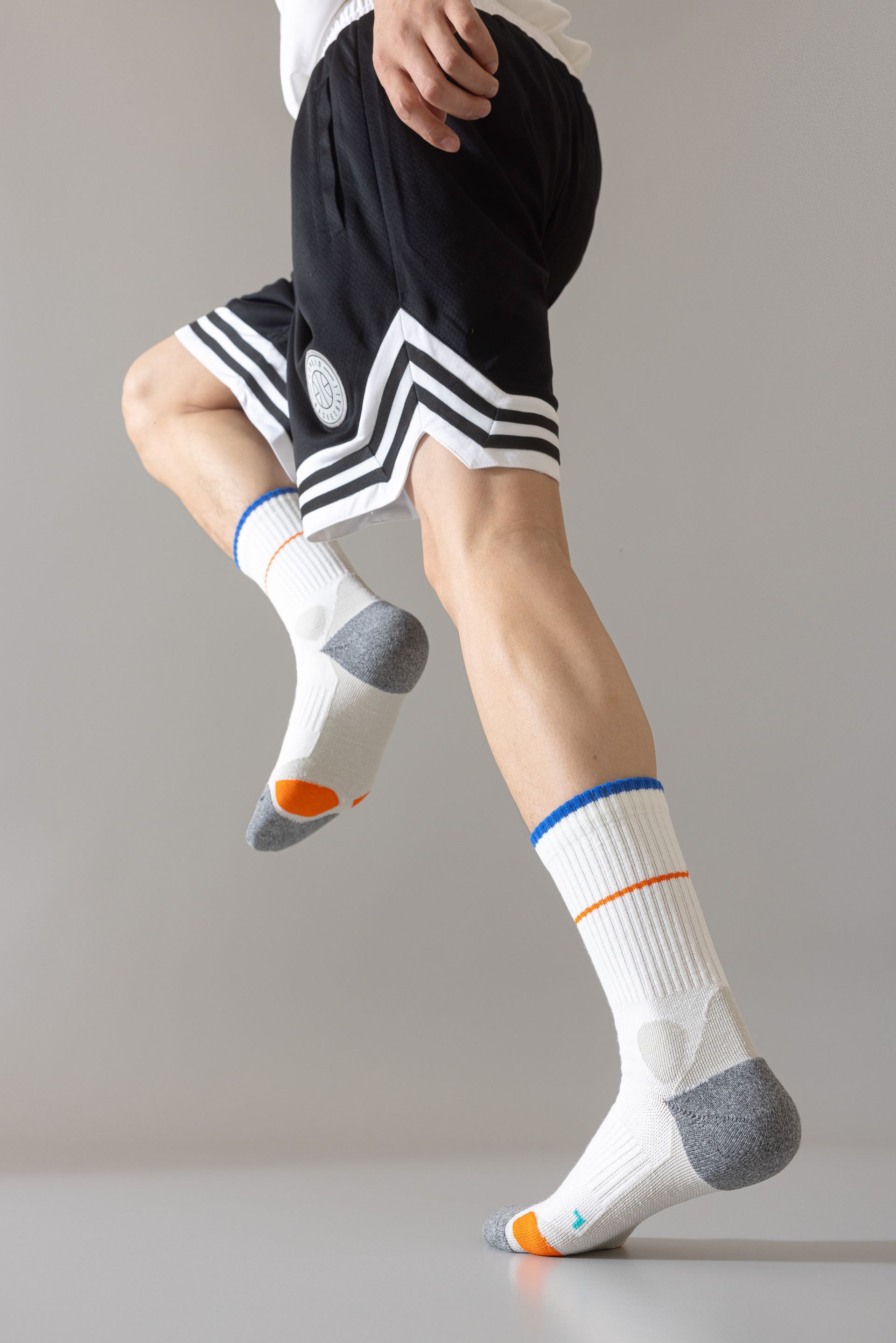 Person running, wearing black shorts, white socks with orange and grey accents. Light grey background.
