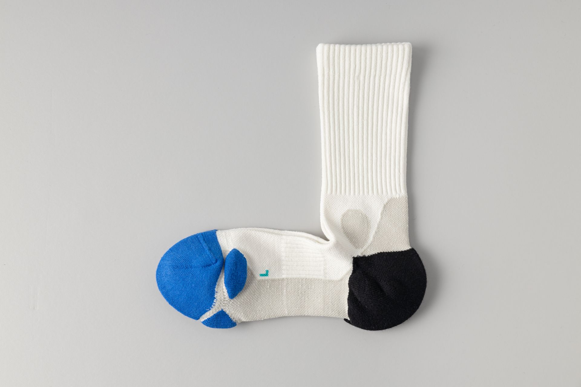 White sock with blue toe and black heel, lying on a gray surface.