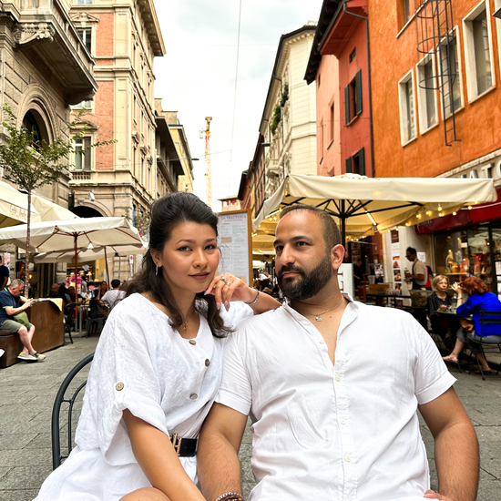 Couple smiling outdoors in Italy. Woman in white dress, man in white shirt, seated in a square.