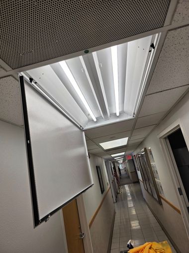 Narrow office hallway with fluorescent lights, white walls, and a hanging projector screen on the left.
