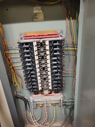 Electrical breaker panel with rows of switches and multicolored wires inside a gray metal cabinet