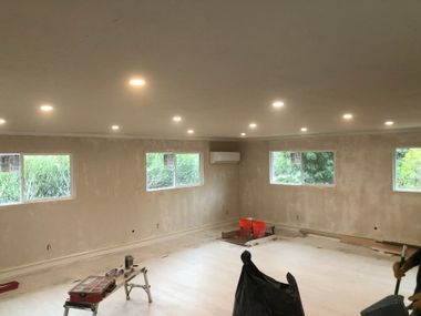 Unfinished room with recessed lights, windows, and construction tools on a bare floor.