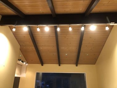 Wood-paneled vaulted ceiling with exposed beams and hanging track lights above a room interior