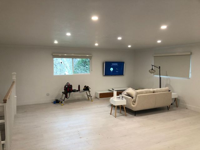 Bright modern living room with white sofa, wall TV, windows, and recessed ceiling lights.