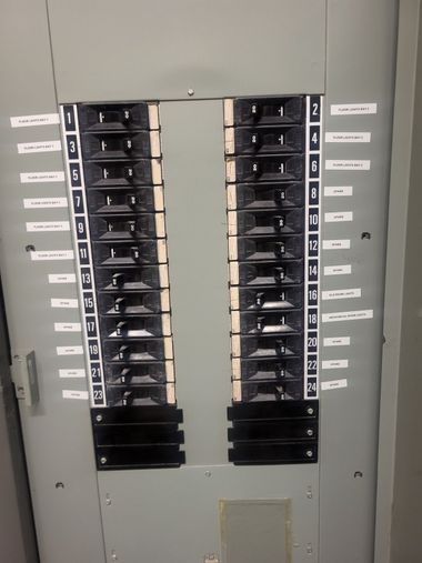 Gray electrical breaker panel with rows of switches and labels on either side.