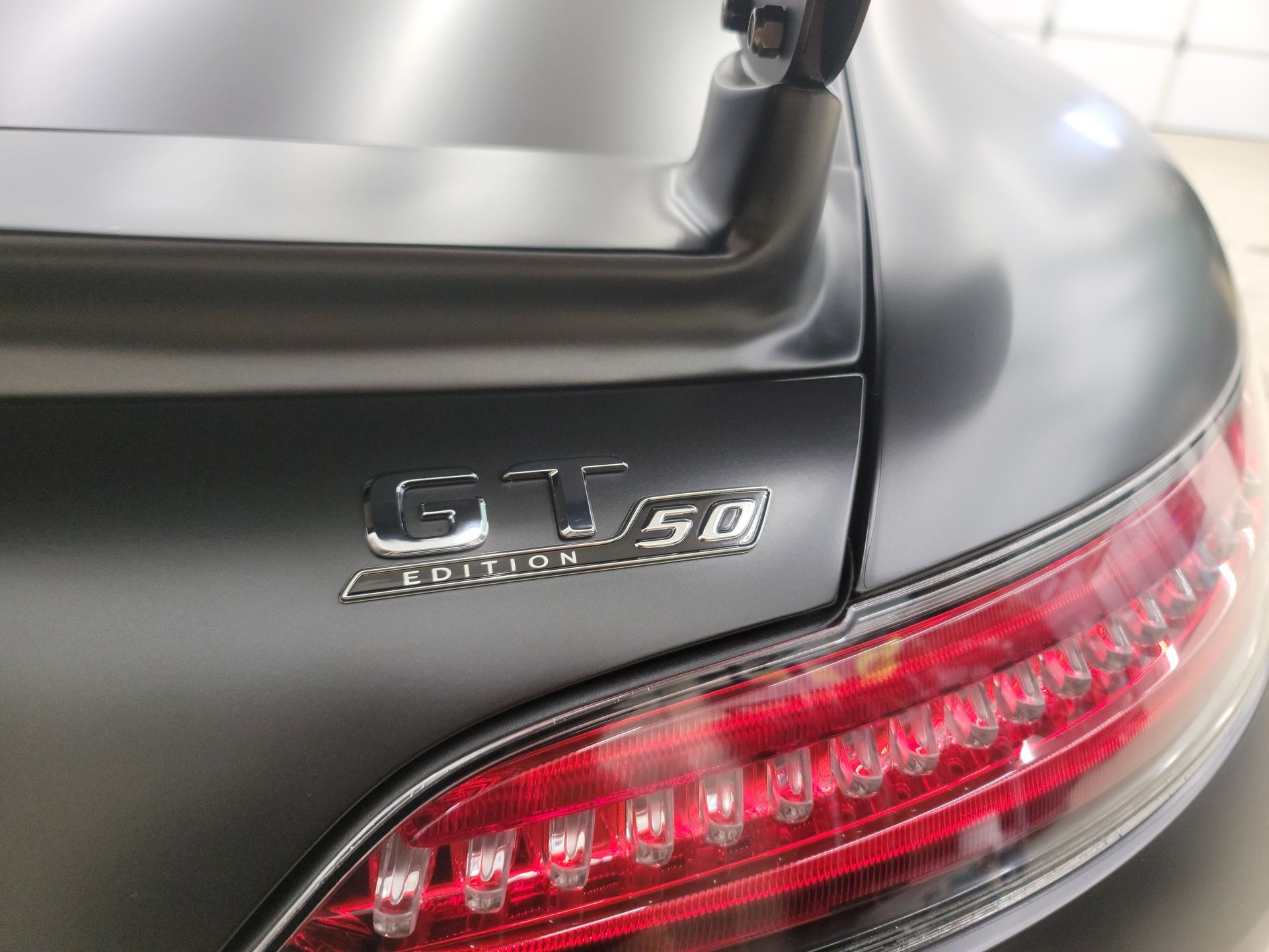 Man in black hat and gloves wiping a shiny black car with a green cloth in a garage.