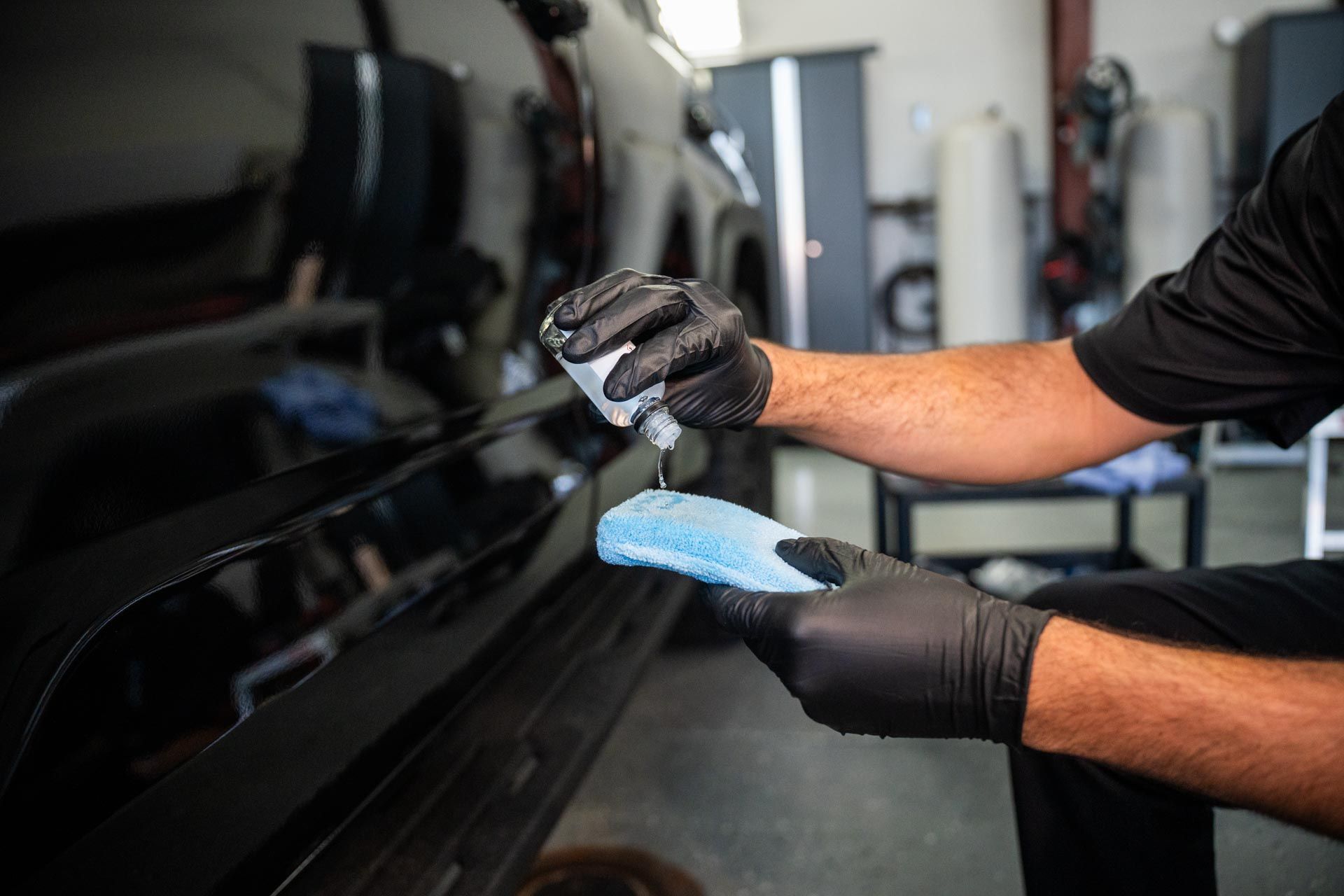 Person wearing gloves applying liquid to a car with an applicator.