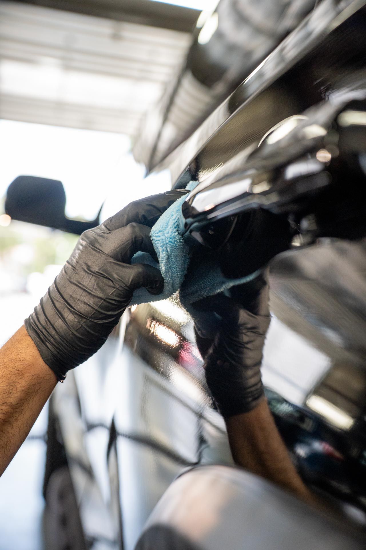 Person wearing black gloves wiping a black car door with a blue cloth.