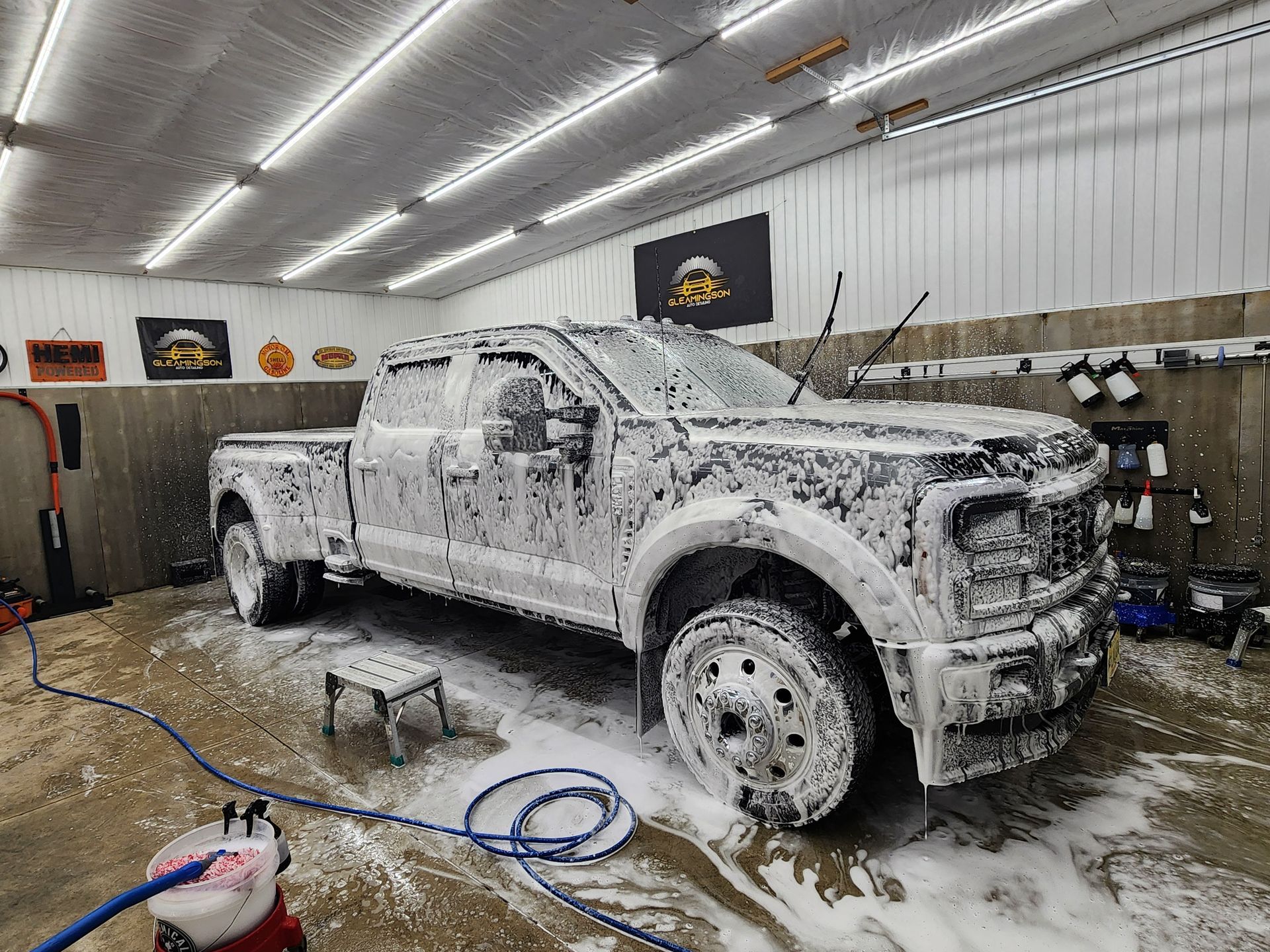 A black Ford pickup truck covered in white foam in a car wash bay.