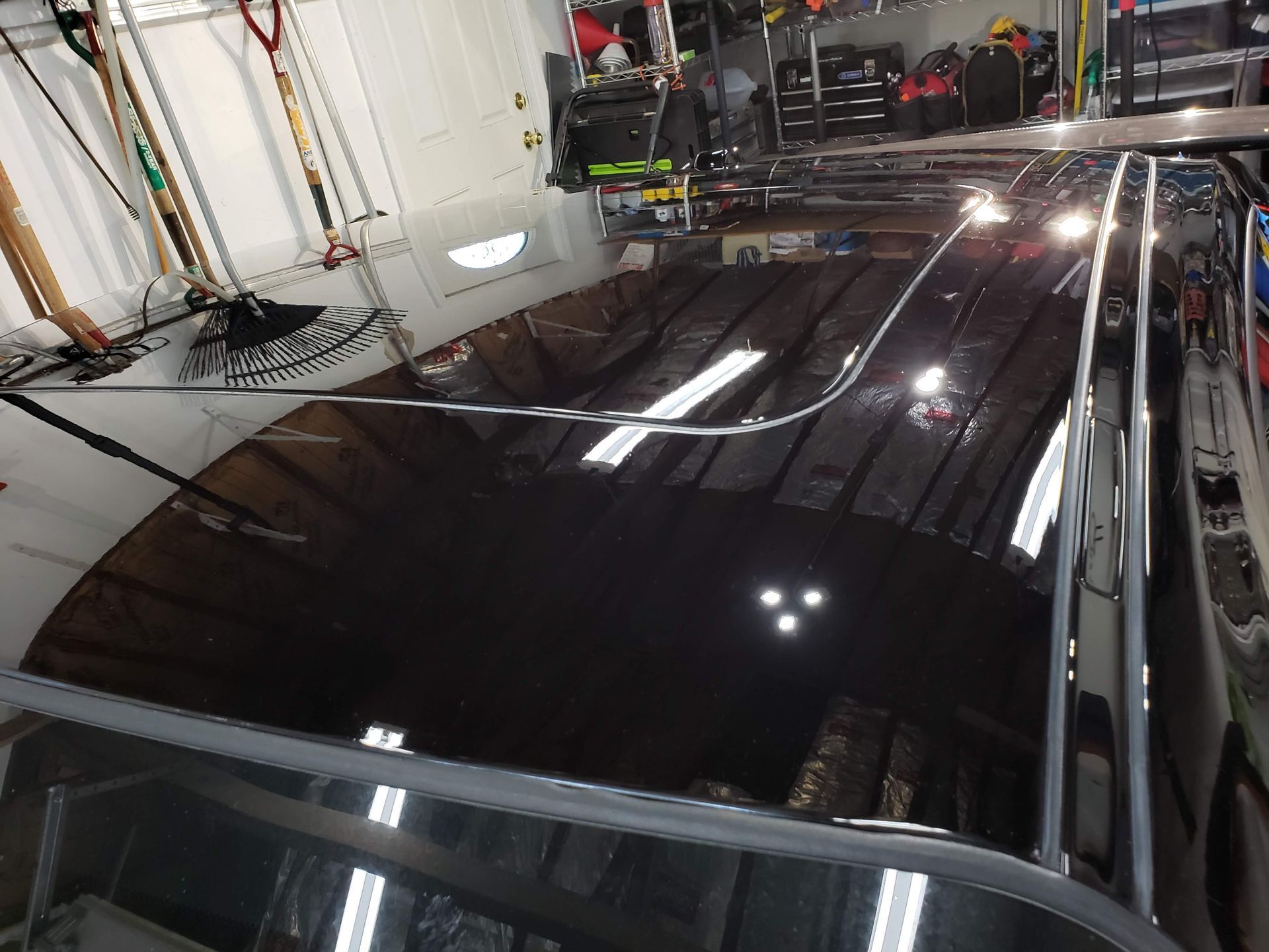 Shiny black car roof reflecting lights in a garage setting.