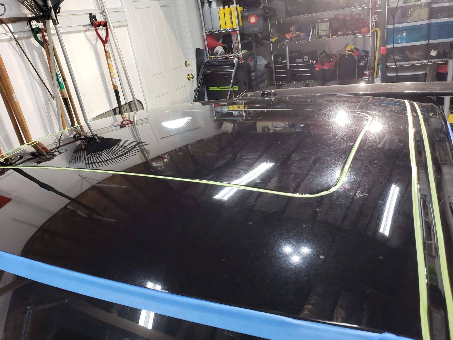 Black car roof being polished, sectioned off with yellow tape, in a well-lit workshop.