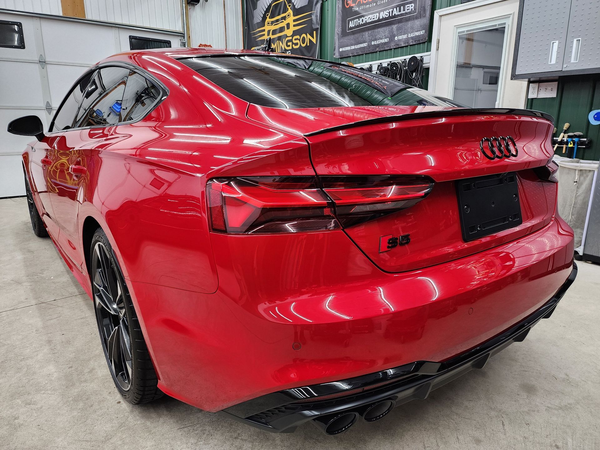 Red Audi S5 coupe, black spoiler, black wheels, garage setting.