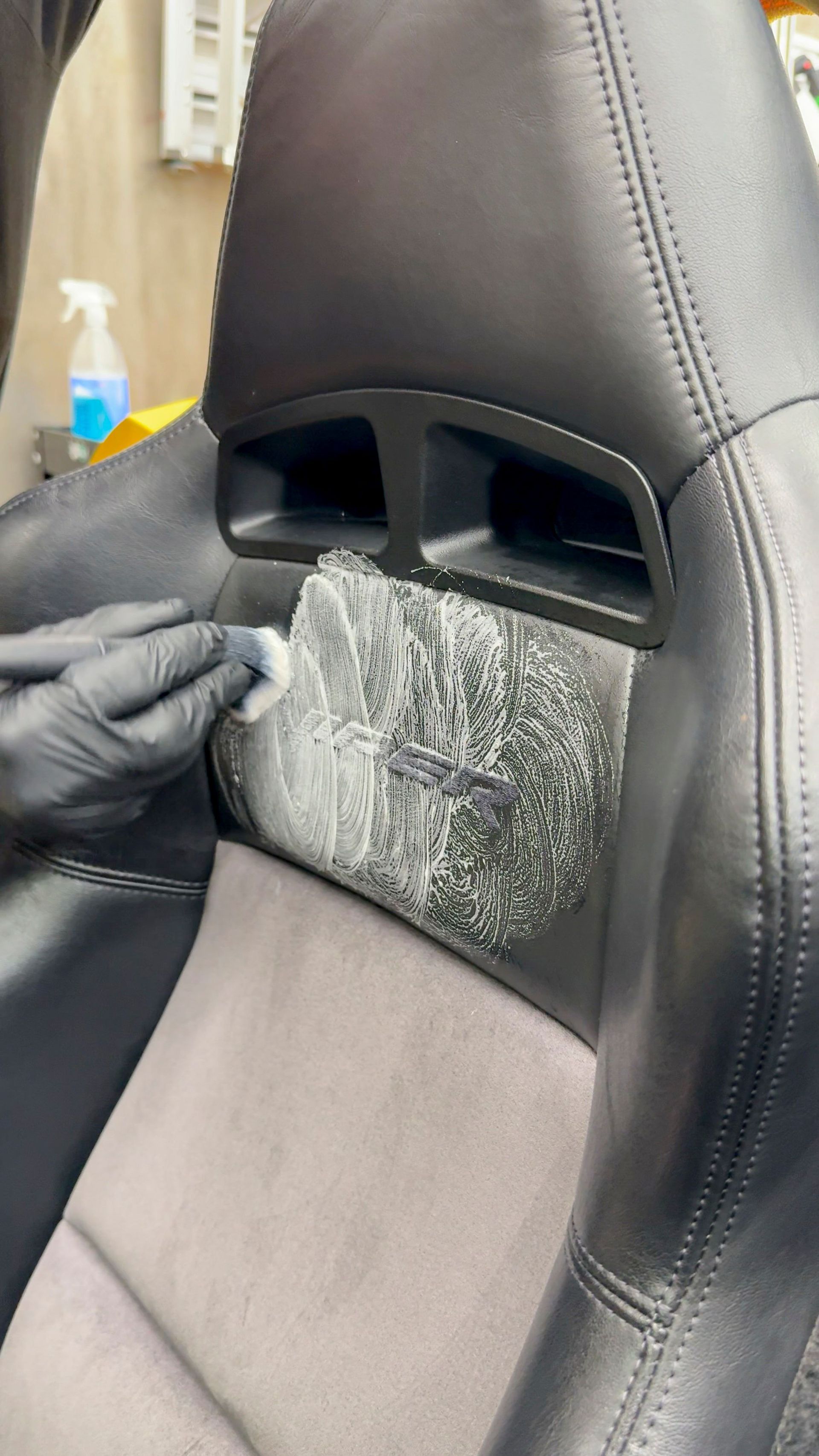 Person with black gloves applying cleaning product to a black car seat.