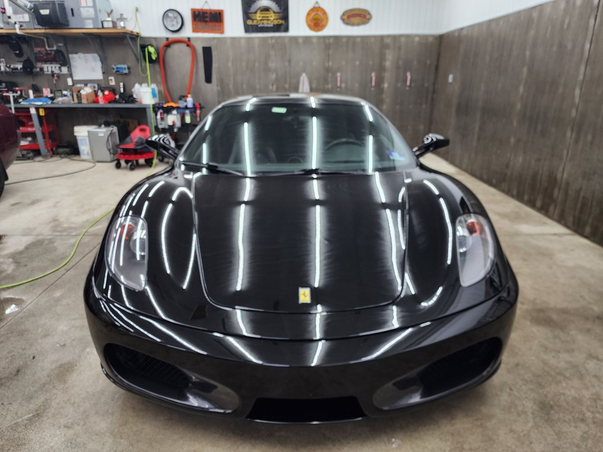 Black Ferrari F430 sports car inside a garage with bright lights.
