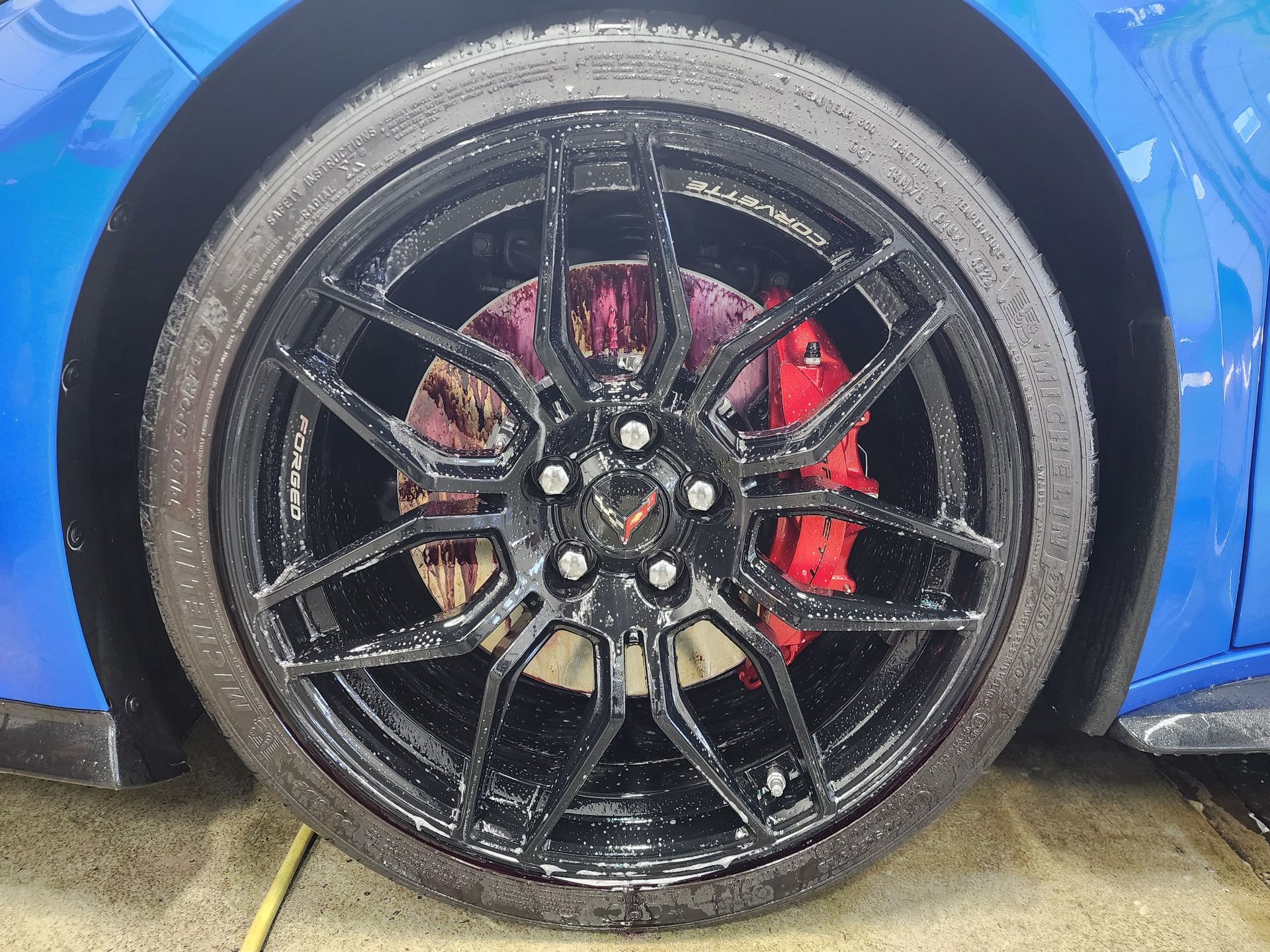 Black car wheel with red brake calipers on a blue vehicle.
