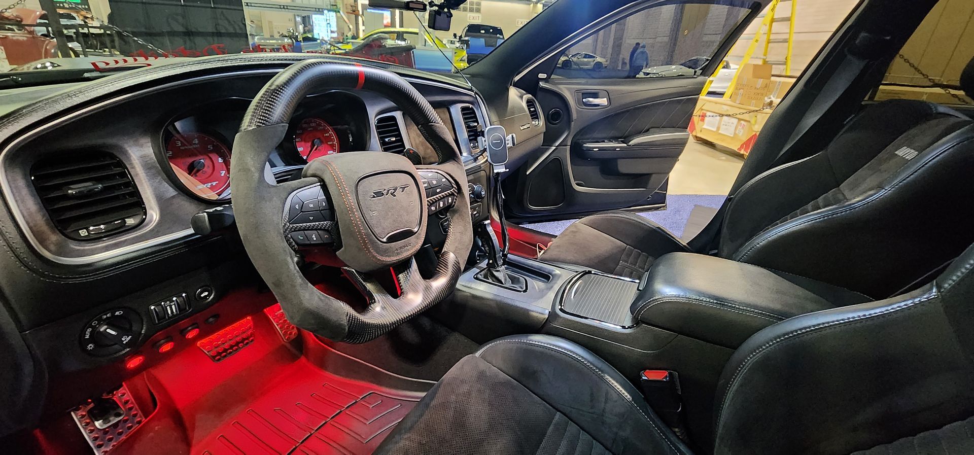 Interior of a Dodge Charger with red lighting, custom steering wheel, and black leather seats.