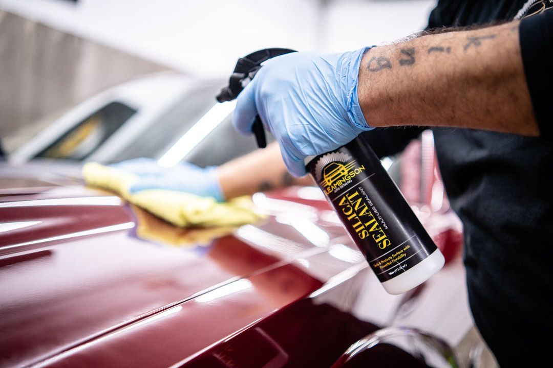 Person spraying car sealant on a red car with a gloved hand.