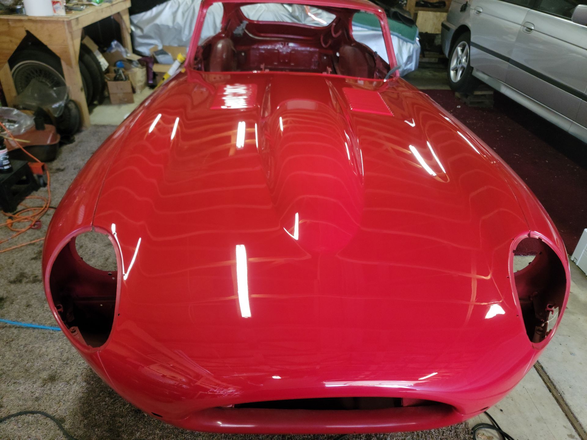 Red sports car body with open headlights, shiny finish, indoors.