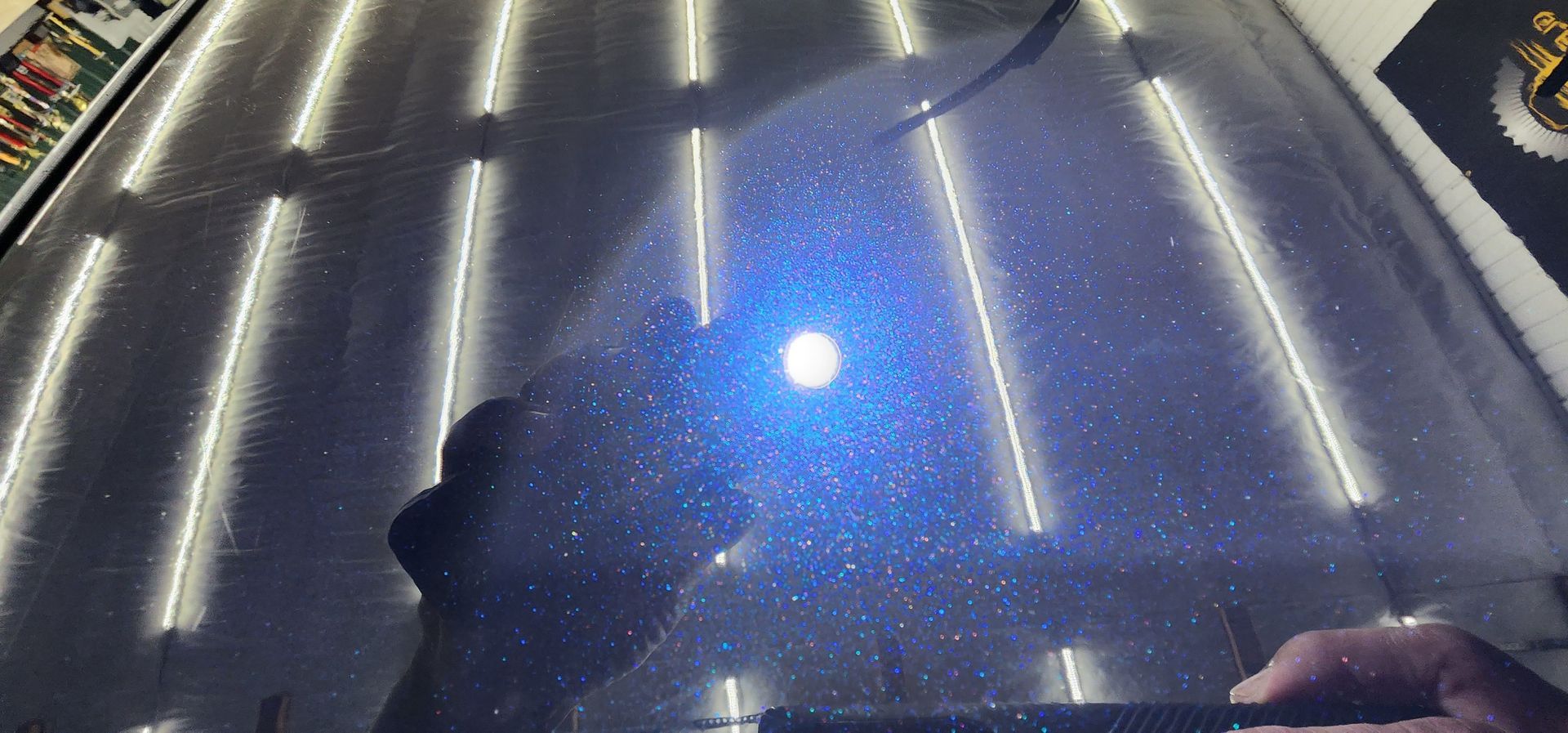 Close-up of a dark, shiny car surface with light reflections. Visible hand with a dark, sparkly effect.