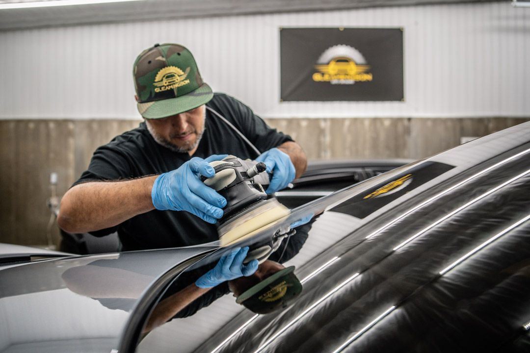 Man wearing a cap polishes a car's surface with a machine.