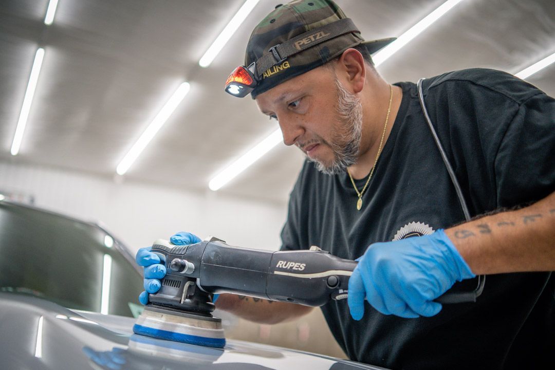 Man polishing car with a power buffer, wearing gloves and a headlamp.