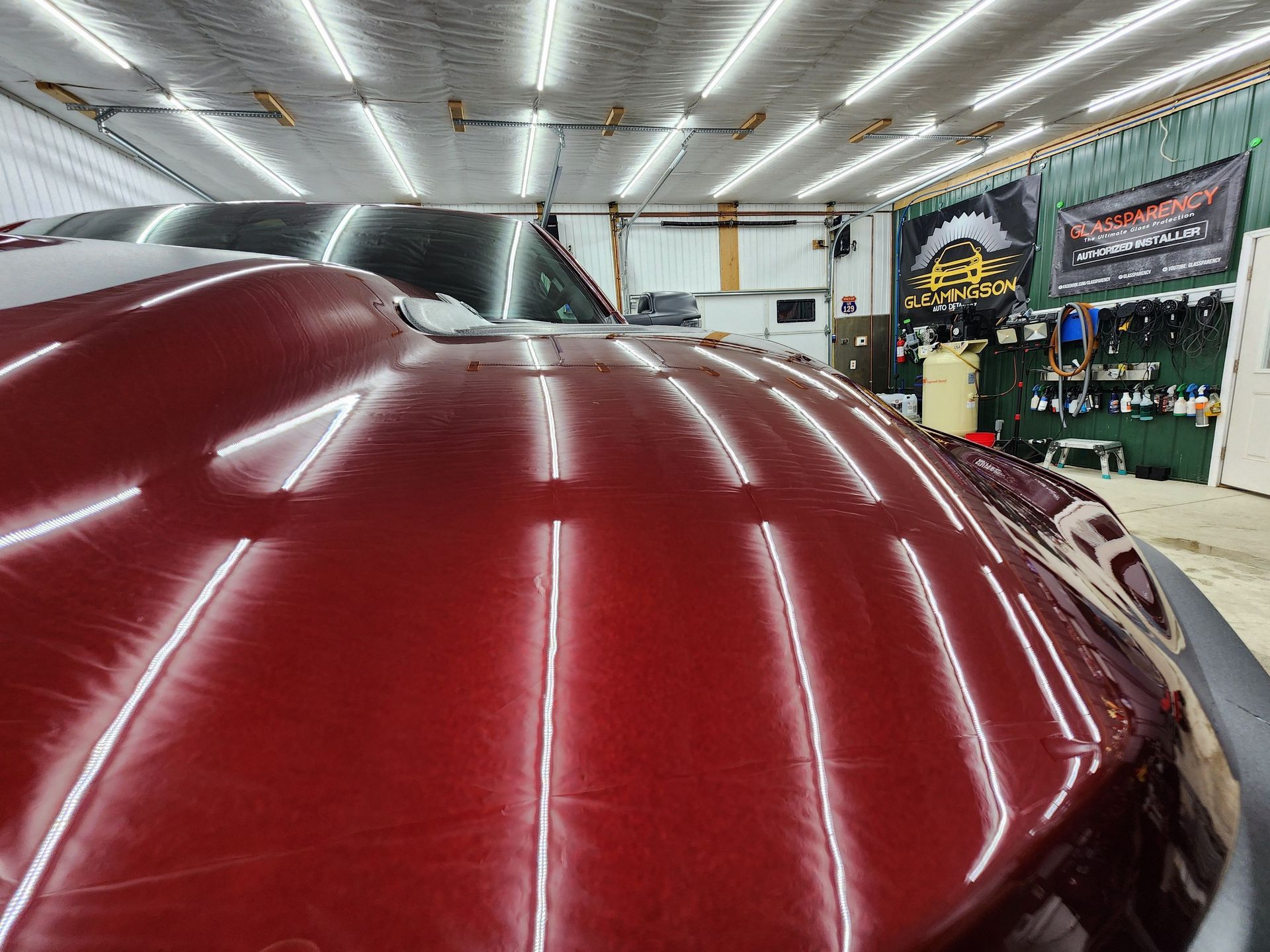 Red car hood with multiple light reflections, inside a shop.