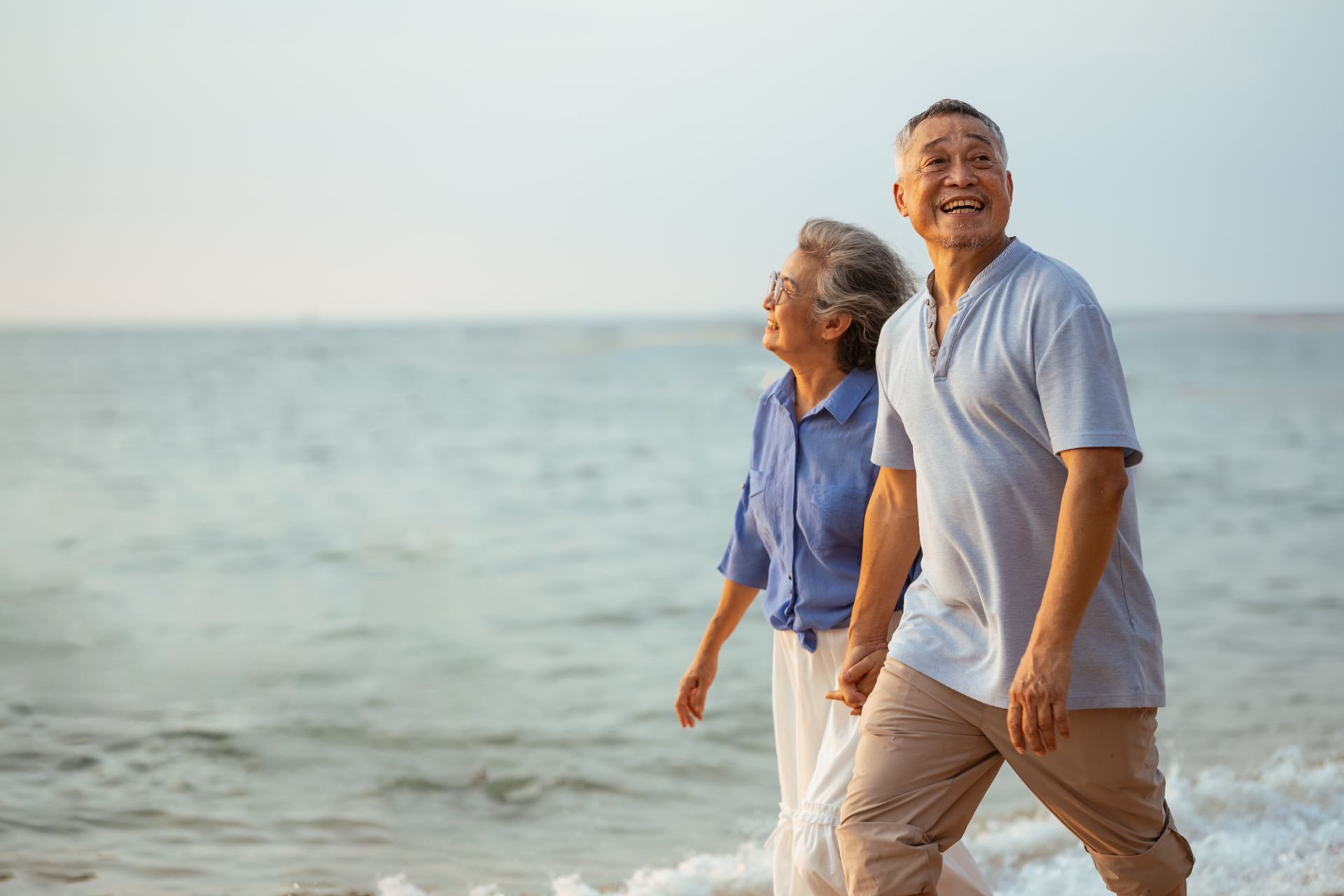 Two people walking along the beach, smiling near the ocean at sunset